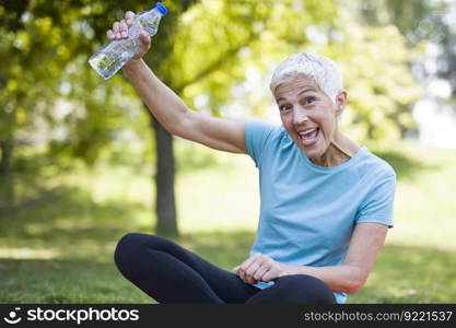 Portrait of smiling senior woman relaxing after exercising while sitting on grass