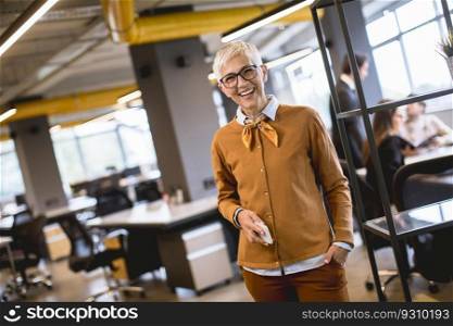 Portrait of smiling senior woman standing in meeting room with team discussing work in background