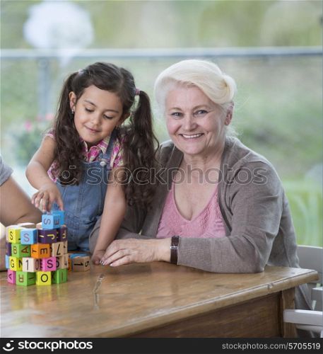 Portrait of smiling senior woman with granddaughter playing with alphabet blocks at home