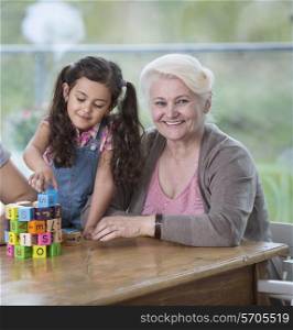 Portrait of smiling senior woman with granddaughter playing with alphabet blocks at home