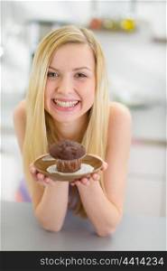 Portrait of smiling smiling teenager girl holding chocolate muffin in kitchen