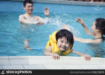 Portrait of smiling son in the water and holding onto the pools edge with family in the background