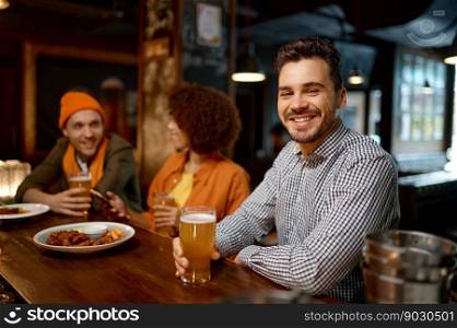 Portrait of smiling sports fan sitting counter desk. Handsome cheerful man drinking craft beer and looking at camera while rest with friends in sport bar. Happy smiling man sitting at sports bar counter desk looking at camera