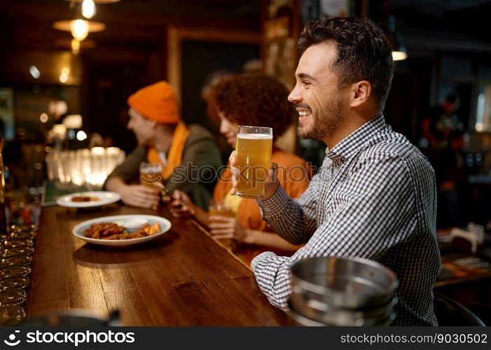 Portrait of smiling sports fan sitting counter desk. Handsome cheerful man drinking craft beer while rest with friends in sport bar. Happy smiling man sitting at sports bar counter desk looking at camera