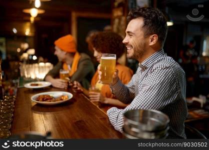 Portrait of smiling sports fan sitting counter desk. Handsome cheerful man drinking craft beer while rest with friends in sport bar. Happy smiling man sitting at sports bar counter desk looking at camera