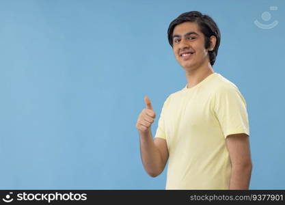 Portrait of smiling teenage boy gesturing while standing against blue background