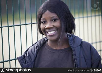 Portrait Of Smiling Teenage Girl Leaning Against Fence Outdoors In Park