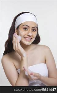 Portrait of smiling woman applying soap on face against white background