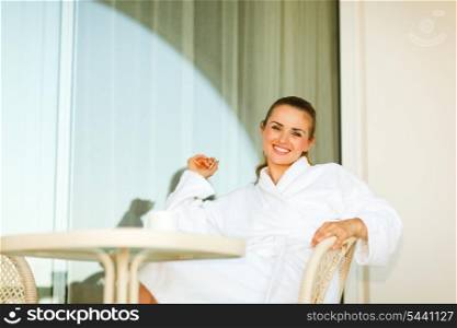 Portrait of smiling woman in bathrobe sitting at table on terrace