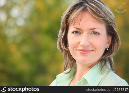 portrait of smiling woman in early fall park. she is looking at camera.