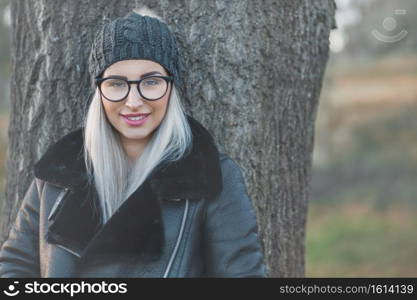 Portrait of smiling woman in warm clothing on winter day outdoors. Happy girl wearing wool cap and black jacket. Female person in cold weather.