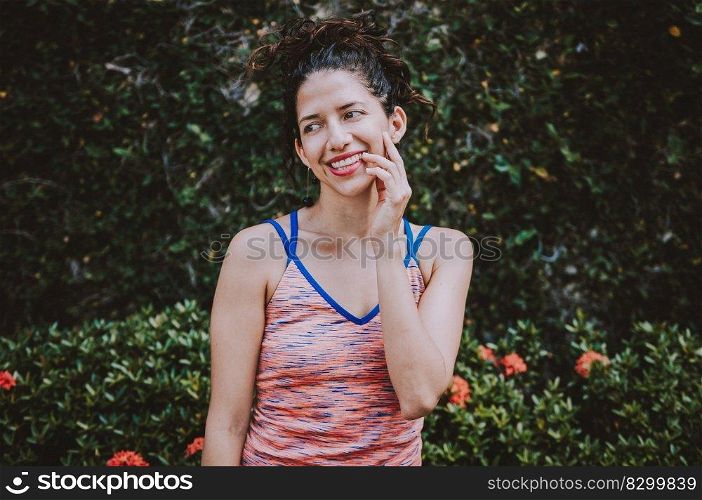 Portrait of smiling woman near a grass wall. Close-up of happy girl near a garden outdoors. Smiling latin woman near a garden with defocused background