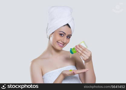 Portrait of smiling woman pouring beauty product on palm over gray background