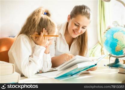 Portrait of smiling woman reading book with daughter at desk