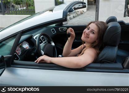 Portrait of smiling woman sitting in convertible car and holding car keys