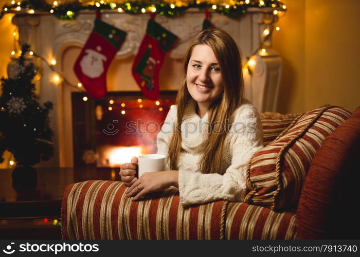 Portrait of smiling woman sitting on chair at fireplace and drinking tea