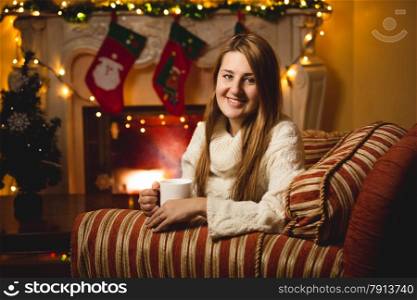 Portrait of smiling woman sitting on chair at fireplace and drinking tea