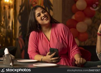 Portrait of smiling woman using mobile phone while sitting at restaurant
