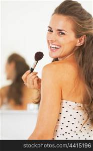 Portrait of smiling woman with makeup brush in bathroom