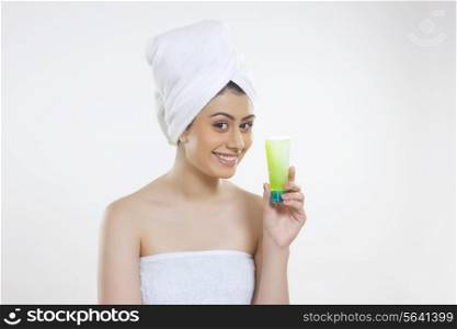Portrait of smiling woman wrapped in towel holding beauty product against white background