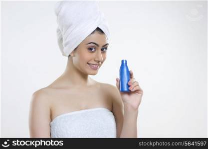 Portrait of smiling woman wrapped in towel holding hair oil bottle against gray background