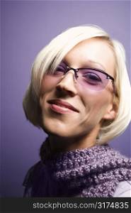 Portrait of smiling young adult Caucasian blond woman on purple background wearing sunglasses and scarf.