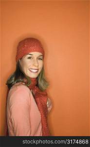 Portrait of smiling young adult Caucasian woman on orange background wearing winter hat and scarf.