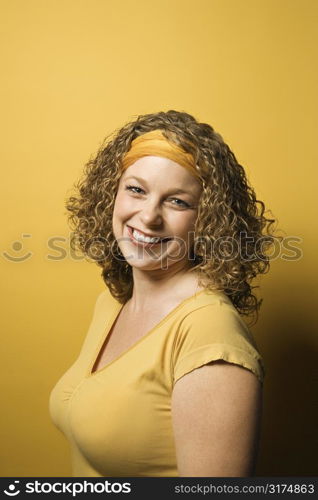 Portrait of smiling young adult Caucasian woman on yellow background.