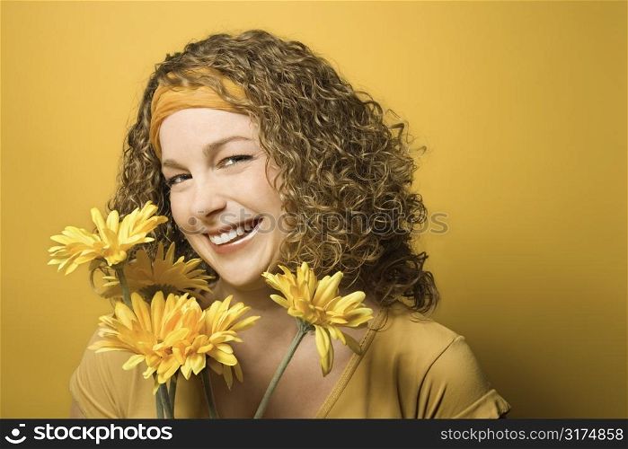 Portrait of smiling young adult Caucasian woman on yellow background holding bouquet of flowers.