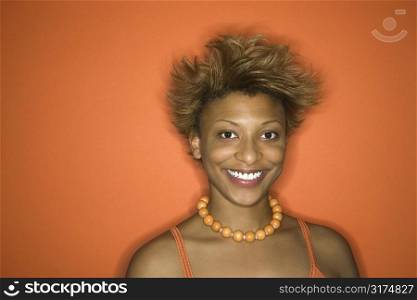Portrait of smiling young African-American adult woman on orange background.