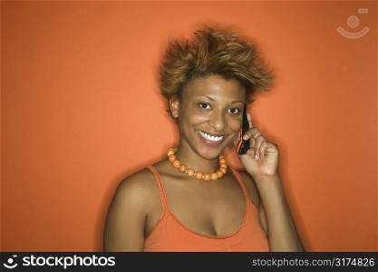 Portrait of smiling young African American adult woman on orange background talking on cellphone.