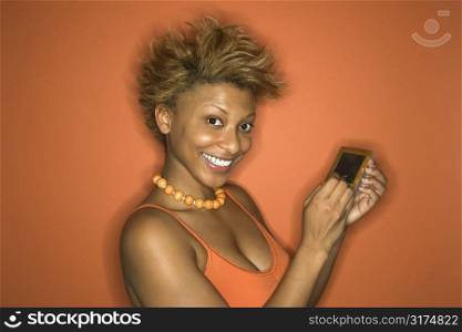 Portrait of smiling young African-American adult woman on orange background using her palmtop computer.