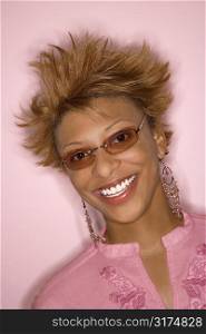 Portrait of smiling young African-American adult woman on pink background wearing sunglasses.