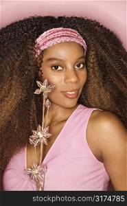 Portrait of smiling young African-American adult woman with big hair on pink background holding glass bead flowers.