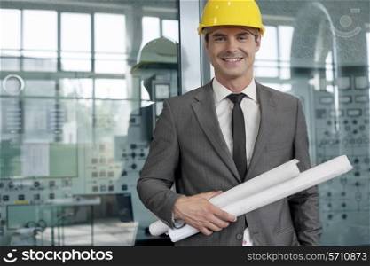 Portrait of smiling young architect holding rolled up blueprints in industry