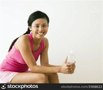 Portrait of smiling young Asian woman holding bottle of water.