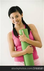 Portrait of smiling young Asian woman holding exercise mat.