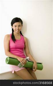 Portrait of smiling young Asian woman holding yoga mat.
