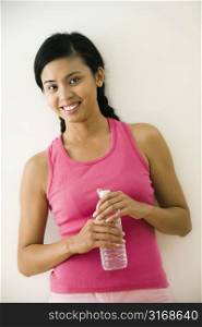 Portrait of smiling young Asian woman standing in fitness clothes holding bottle of water.