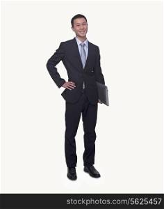 Portrait of smiling young businessman holding a laptop, hand on hip, studio shot