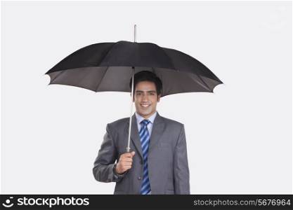 Portrait of smiling young businessman holding umbrella over gray background