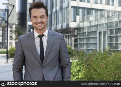 Portrait of smiling young businessman standing against office building