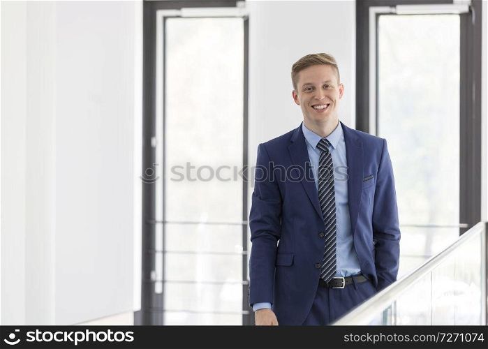Portrait of smiling young businessman standing against window at office