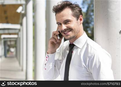 Portrait of smiling young businessman using cell phone outside office