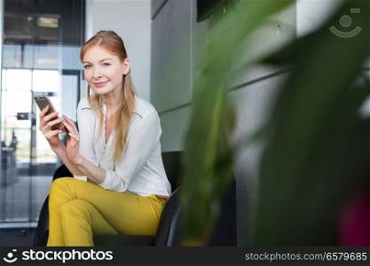 Portrait of smiling young businesswoman using mobile phone on chair in office