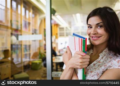 Portrait of smiling young businesswoman with books in office