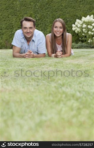 Portrait of smiling young couple lying side by side on grass in park