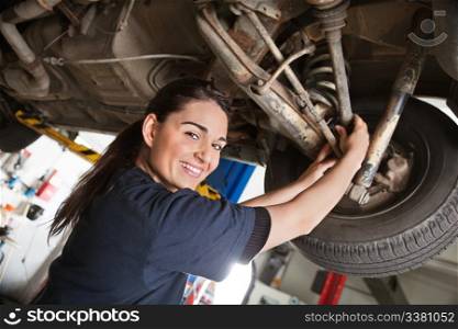 Portrait of smiling young female mechanic inspecting a CV joing on a car in auto repair shop