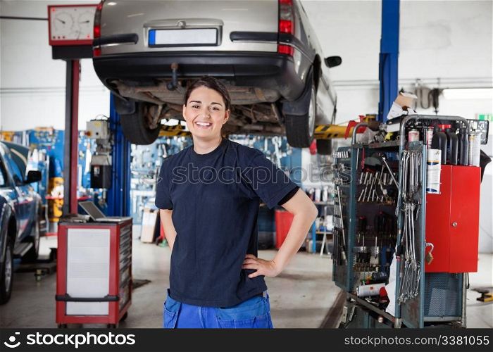 Portrait of smiling young female mechanic with hands on hips in auto repair shop