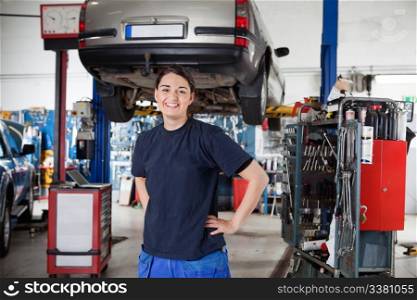 Portrait of smiling young female mechanic with hands on hips in auto repair shop